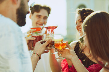 Golden light of sun enhances cheerful toast among friends, their drinks shimmering. Concept of party, Friday mood, alcohol drinks and celebration, summer holidays, relax, rest, youth.