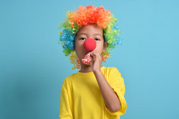 Cute little asian boy with clown wig, clown nose and party whistle isolated on blue background. copy space