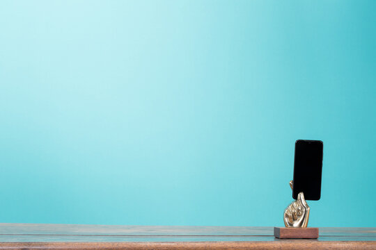 Mobile phone in retro golden arm front gradient mint blue background. Vintage old style filtered photo. Contact numbers banner concept