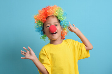 Cute little asian boy with clown wig and clown nose isolated on blue background. copy space
