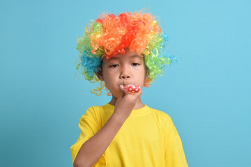 Cute little asian boy with clown wig and party whistle isolated on blue background. Copy space