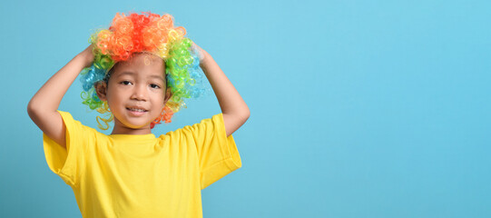 Cute little asian boy in clown wig isolated on blue background. banner design. copy space