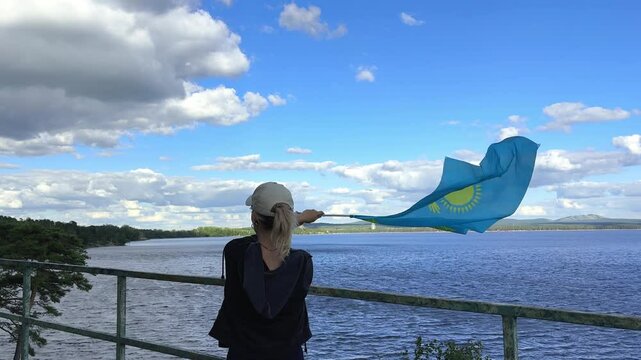 Young woman traveling in the Kazakhstan. She is standing by back and holding the blue of Kazakhstan Republic. Borovoe lake view. 