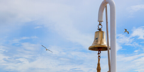 Ship's bell on a white mast against a blue sky with seagulls, sea travel, ocean vacation
