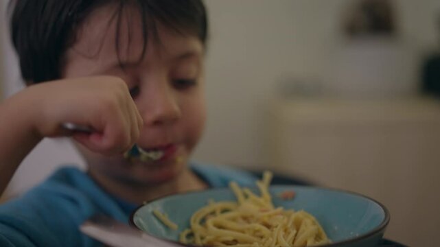 One little boy eating spaghetti noodles for dinner time by himself. Child using fork to eat pasta food