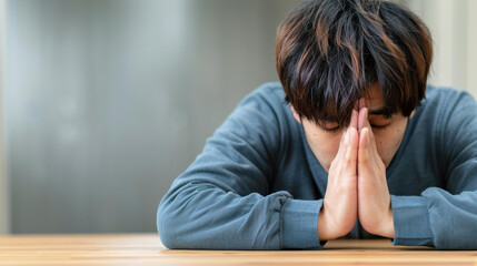 Faithful young man praying on a sofa, seeking luck, success, and forgiveness in his home office. Power of religion and worship.