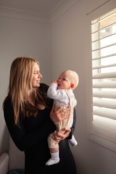 happy young mum with first baby inside home with winter light coming through blinds