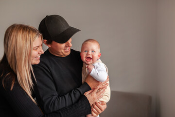 Happy young family smiling together in home dad holding baby boy with big smile