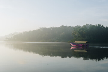 Morning view of a boat is floating on a calm lake with a foggy sky and nature background at Sermo lake, Yogyakarta, Indonesia.