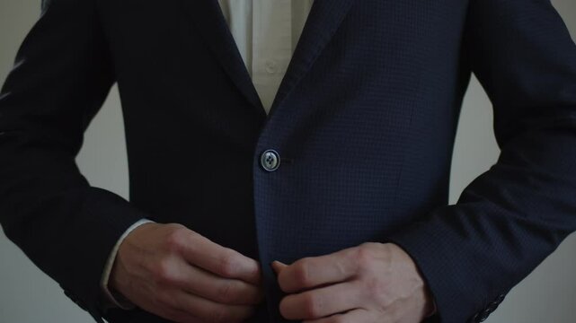 A young adult man fastens the buttons on a business suit on a white background. Close-up of a body part. Front view