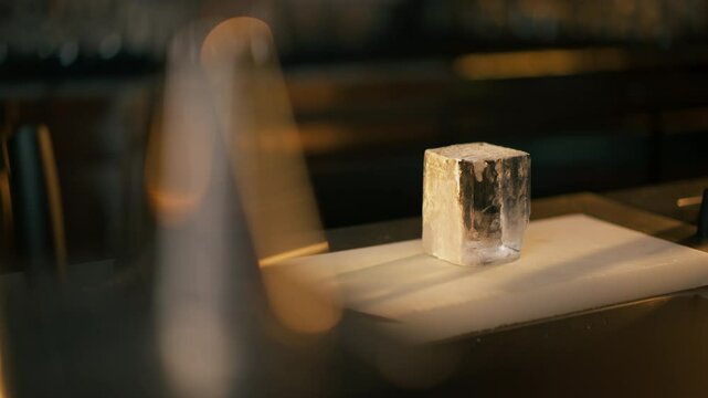 on the bar counter on white board there is a square cut transparent ice for whiskey