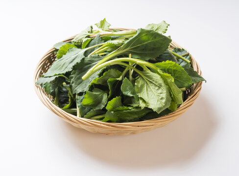 Close-up of stacked raw Chwinamul with leaf and stem on bamboo basket and white floor, South Korea
