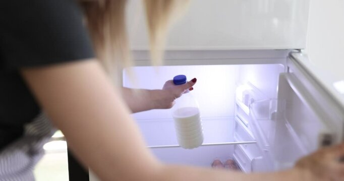 Housewife in apron opens fridge putting bottle with milk