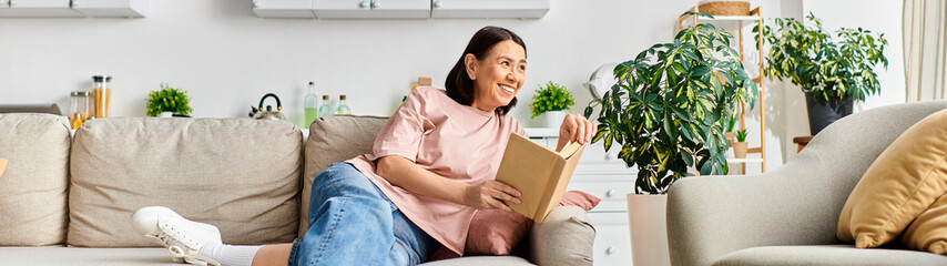 A mature woman in comfortable homewear sitting on a couch, lost in a book.