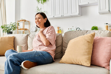 A mature woman in cozy homewear sitting on a couch, enjoying a cup of coffee.