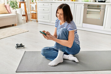 A mature woman in cozy homewear sitting on the floor, engrossed in her phone.