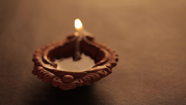 A backlit earthen oil lamp being lit by a male hand during Diwali, creating a warm and festive atmosphere.