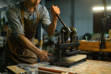 Leather craftsman working with manual leather die cutting machine in his workshop.