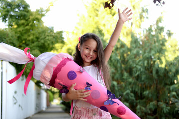 Little girl  with school satchel on first day to school, holding school cone with gifts