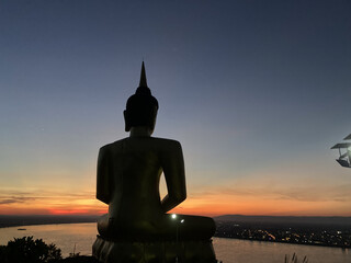 Buddha statue situated on a mountain, gazing at a breathtaking sunset over a peaceful river