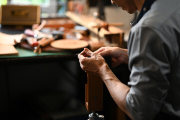 Young leather craftsman carefully stitching leather pieces. Small business and handmade concept