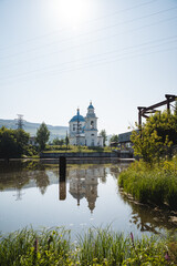 Obraz premium The serene church is mirrored in the placid lake, forming a peaceful and delightful scenery. Water, sky, plants, and buildings blend in the natural landscape of this tranquil setting