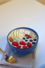 Bowl filled with healthy smoothie, fruit pieces and nuts on the table. Selective focus.