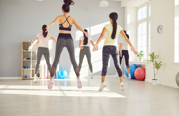 Team of woman athletes is doing jumping exercises together in a gym. Synchronized workout shows the...
