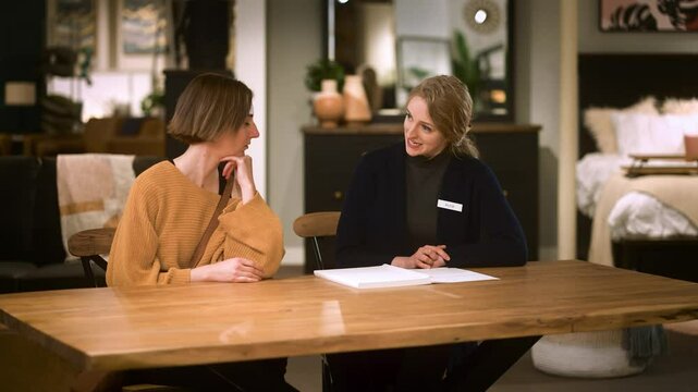 Two Women Sit and Compare Offers Sales Associate and Customer in Store