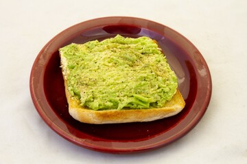 Avocado pear with black pepper and salt on a slice of white bread toast