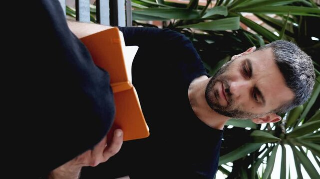 Vertical shot of a man with short dark hair and a beard, sitting on a park bench and writing reflections in a notebook. The scene highlights his introspection and engagement with personal thoughts.