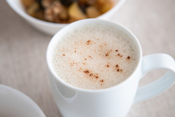 White cup of frothy cappuccino or vegetable drink with cinnamon powder on top to accompany a delicious and healthy breakfast.