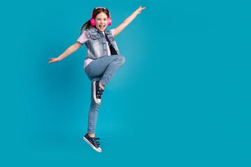 Full length photo of adorable small girl headphones dancing listen music dressed stylish denim garment isolated on blue color background