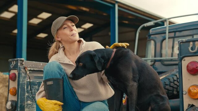 Female farm worker sitting on tailgate of off road farm vehicle with working dog - shot in slow motion