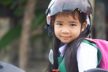 A headshot portrait of a Asian woman, a cute with adorable Wearing a helmet and carrying a pink bag while going to school.a child wearing a student form set smiling and looking to the camera.