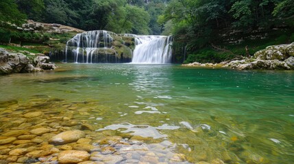 A beautiful waterfall is surrounded by rocks and trees. The water is crystal clear and the rocks are scattered throughout the area. The scene is peaceful and serene