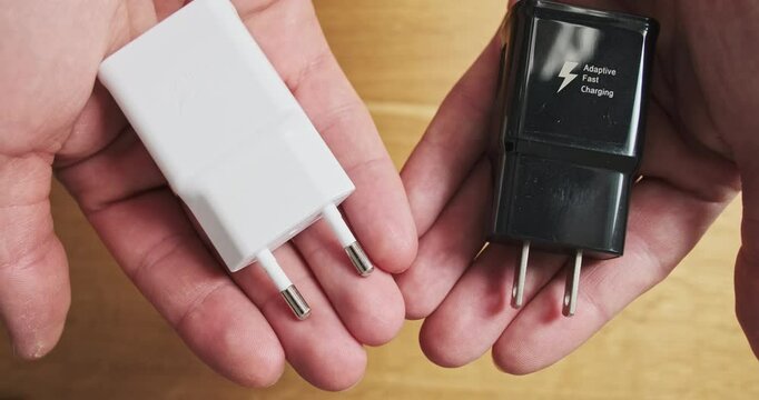 Hands show two chargers with different types of plugs to choose from. Two identical charging adapters with a European and American plug.