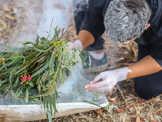 Human hands with green branches, wooden ritual dish and fire, Australian aboriginal smoking ceremony, indigenous event
