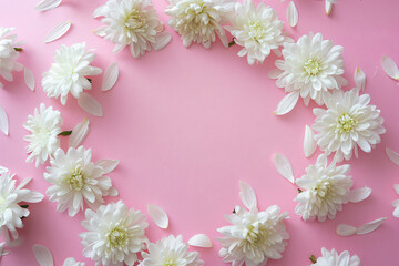 Obraz premium A white chrysanthemum wreath on a pink background with petals in a flat lay top view copy space for text or design.