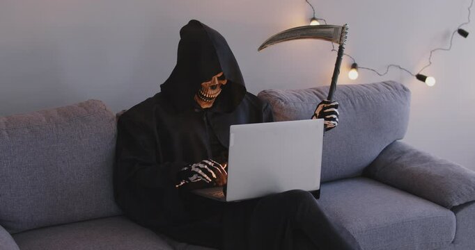 Death uses laptop online on Halloween. The demon communicates while sitting on the couch via web chat on the computer. Grim Reaper.