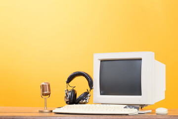 Retro PC monitor, golden microphone, headphones, keyboard and mouse from circa 1990s on oak wooden...