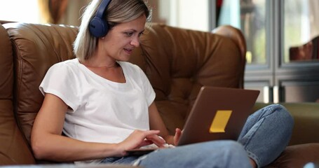 Freelancer woman with headphones and laptop works online sitting on couch. Remote learning of foreign languages