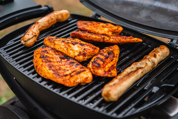 Delicious Chicken Steaks and Sausages Getting Grilled on a Hot Black Grill Grate off a Garden Grill
