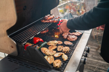 Person Grilling Meat and Vegetables on a Big Home Gas Grill with Hot Flames During Summer Season on a Sunny Day