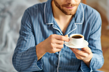 A handsome man in pajamas peacefully enjoying a cup of coffee.