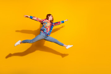 Obraz premium Full size photo of cheerful positive girl dressed print shirt jeans jumping run to empty space isolated on yellow color background
