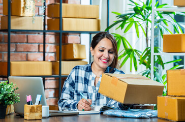 Young Indian asian Female Entrepreneur Handling Online Orders with Laptop and Smartphone in Warehouse