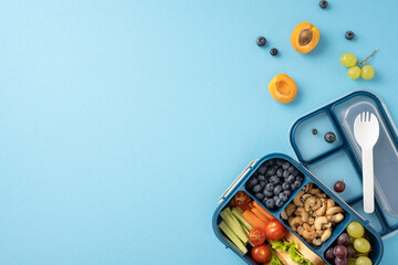 Healthy school lunch with fresh fruits, vegetables, nuts, and a plastic spork in a blue lunchbox...