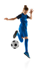 Teen girl in blue uniform in motion, practicing, kicking ball isolated on white studio background. Concept of sport, active and healthy lifestyle, childhood, school, hobby