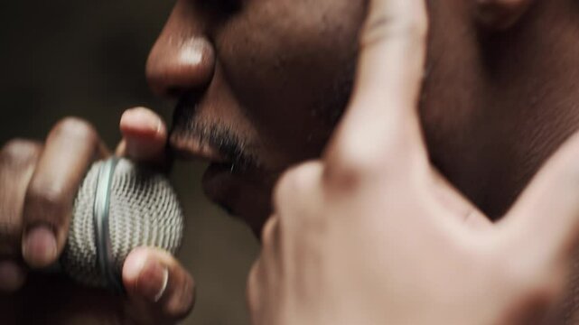 Closeup of Black male rapper gesturing while singing in microphone on stage with flashing lights